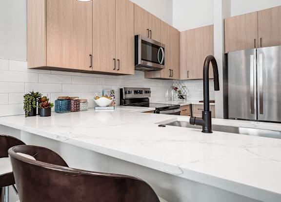 A kitchen with a white countertop and brown chairs.