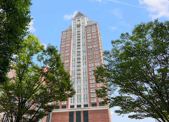 A tall building with a red brick base and a pinkish facade stands between two trees at Residences Providence, Rhode Island