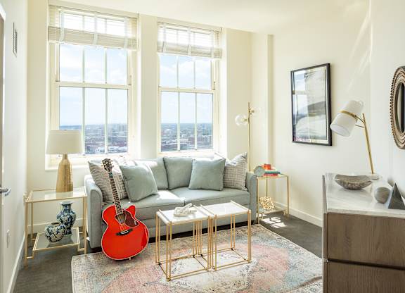A living room with a couch, guitar, and a view of the city at Residences Providence, Rhode Island