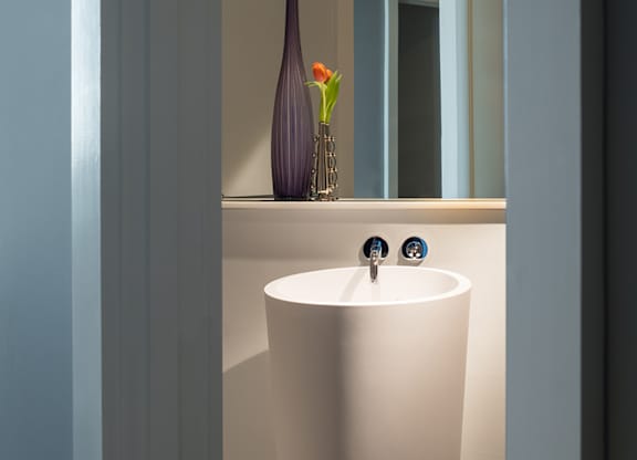 A white pedestal sink with a purple vase with a red flower in it at Residences Providence, Providence, RI 2903