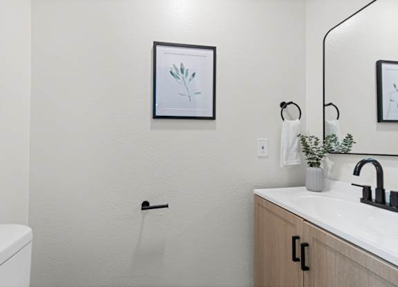 A bathroom with a white toilet, a sink with a black faucet, and a framed picture on the wall.