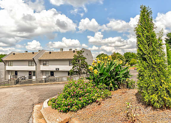 A white building with a grey roof is surrounded by a garden with a variety of plants and flowers.