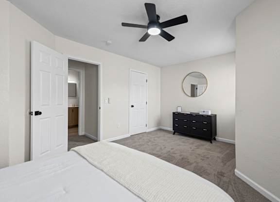 A bedroom with a bed, dresser, mirror, and ceiling fan.