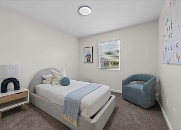 A bedroom with a bed, chair, and a picture on the wall.