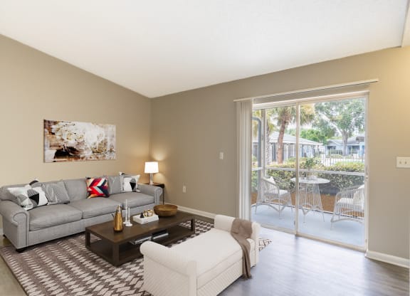 a living room with a couch and a chair and a sliding glass door at Aqua Bay Apartments in Naples, FL 34116