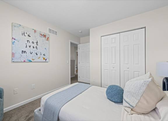 A bedroom with a bed, a blue chair, and a wall hanging with the phrase "it's not just music".