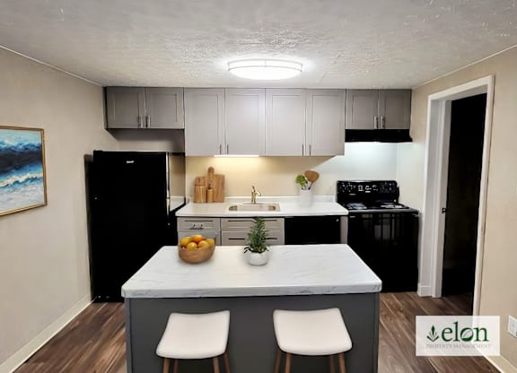 A kitchen with a black refrigerator, white cabinets, and a painting on the wall.