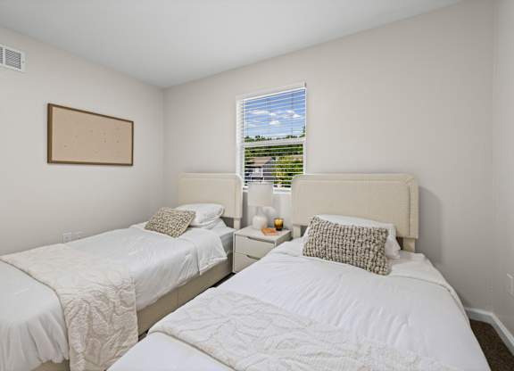 Two white beds in a room with a window showing a view of a highway.