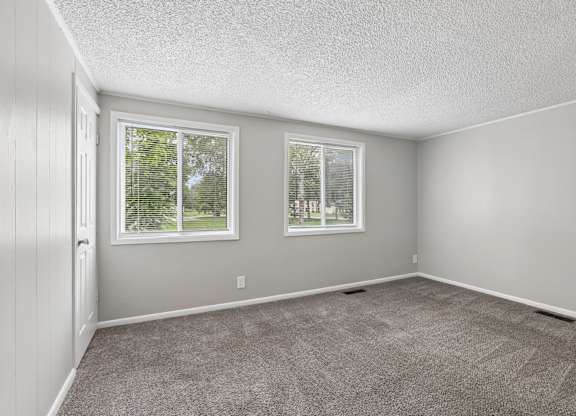 A room with two windows and carpeted floor.
