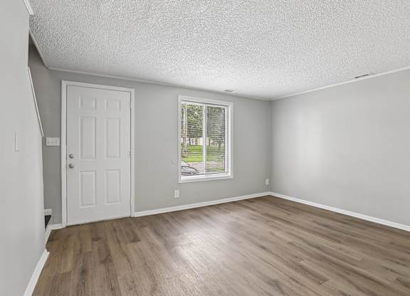 A room with a white door and a window with a view of a tree.