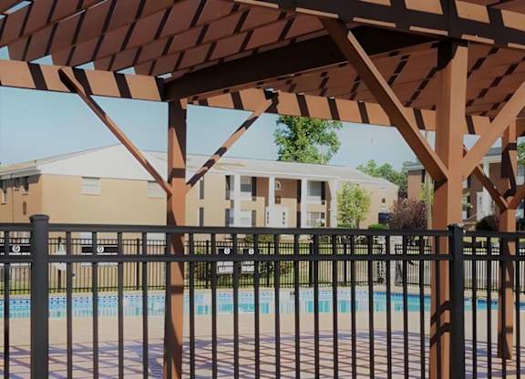 A pool area with a black fence and a brown pergola.