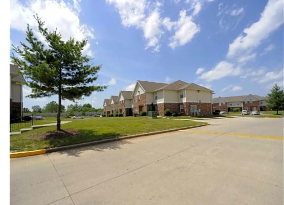 Exterior of Woodhaven Park apartment buildings with parking spots, grass areas, and trees during the daytime.