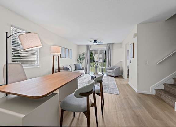 A room with a wooden table and chairs with a staircase in the background.