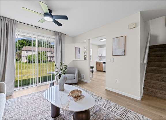 A living room with a fan, a sofa, a table and a staircase.