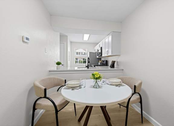 A white dining table with four chairs and a vase of flowers on top.