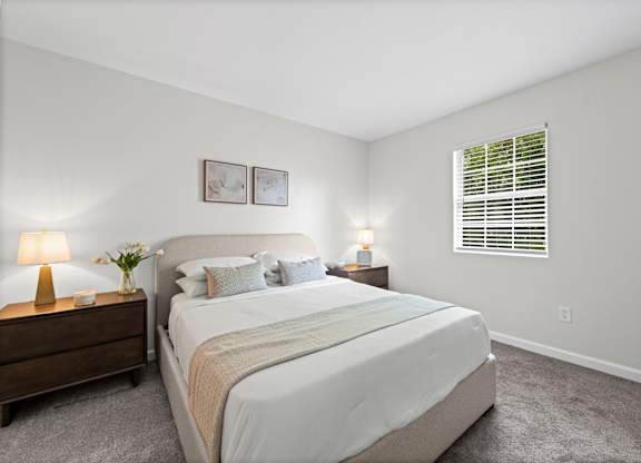 A bedroom with a large bed, two nightstands with lamps, and a window with blinds.