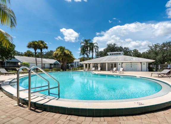 a swimming pool with chairs and a building in the background at Aqua Bay Apartments in Naples, FL 34116