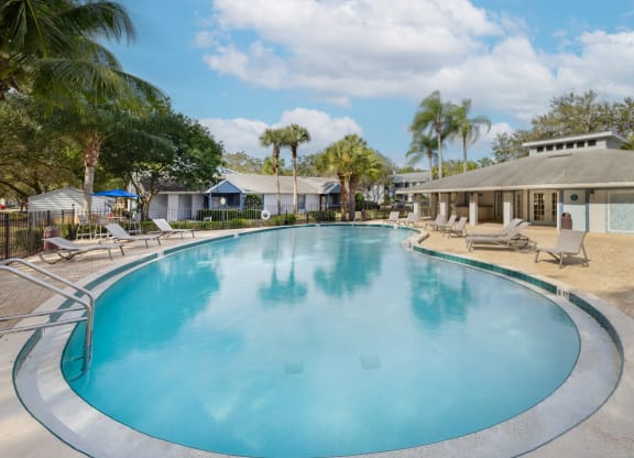 a large swimming pool with chairs and a house in the background at Aqua Bay Apartments in Naples, FL 34116