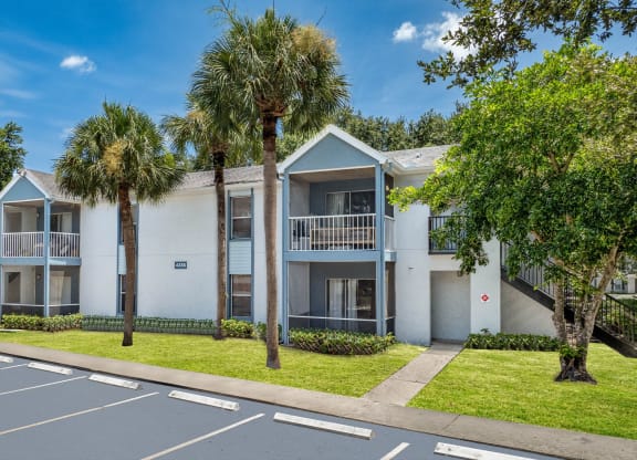 a white apartment building with palm trees in front of it at Aqua Bay Apartments in Naples, FL 34116