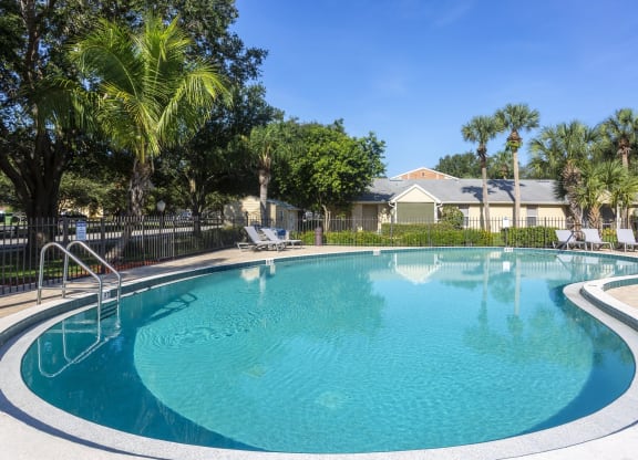 a swimming pool with palm trees and a house in the background at Aqua Bay Apartments in Naples, FL 34116