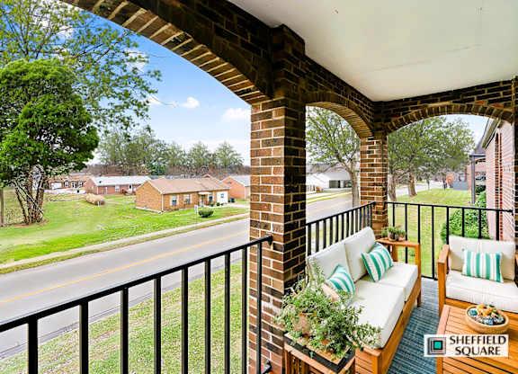 A balcony with a sofa and pillows overlooks a street.