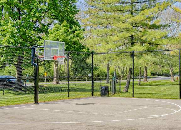 A basketball court surrounded by a fence with a basketball hoop on the left side.