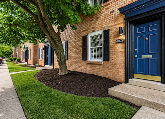 A brick house with a blue door and a tree in front.