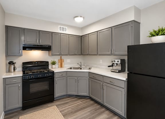 A kitchen with a black refrigerator and grey cabinets.