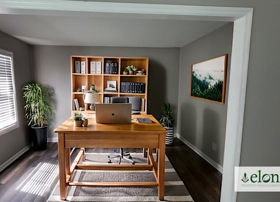 A room with a desk, laptop, and a potted plant.
