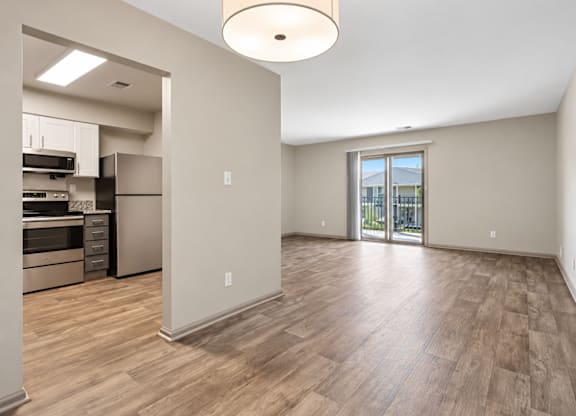A spacious room with wooden flooring and a kitchen area with stainless steel appliances.