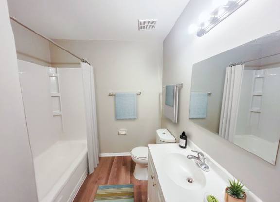 Bathroom with a large mirror, a bathtub, a toilet, and a sink with white countertops. 