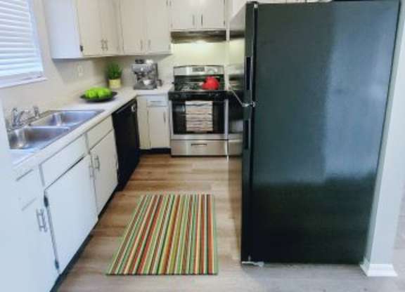 Kitchen area with a fridge, stovetop oven, dishwasher, and white cabinets. 