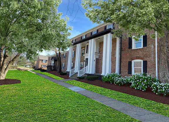 A building with a brick facade and a white trim is surrounded by a well-manicured lawn and trees.