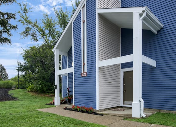 A blue house with a white porch and a brown door.