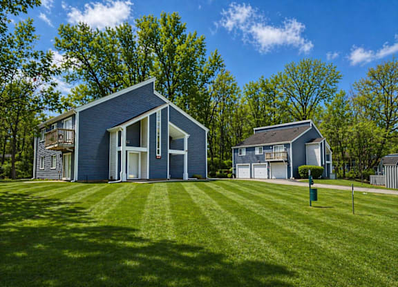 A modern house with a blue exterior is surrounded by a green lawn and trees.