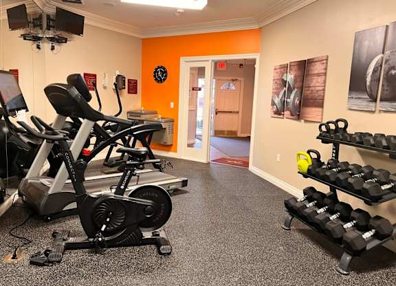 A gym with orange walls and a variety of exercise equipment.