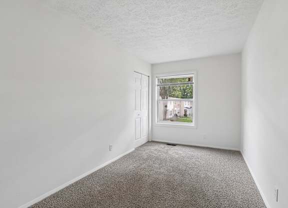 A room with a carpeted floor and a window showing a view of a street with houses.