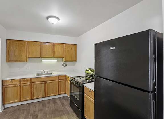 A black refrigerator sits in a kitchen with wooden cabinets.