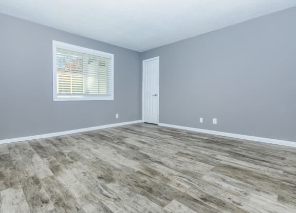 an empty room with wood floors and grey walls and a window
