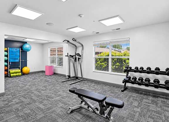 A gym with a variety of equipment including a bench, weights, and a leg press machine.