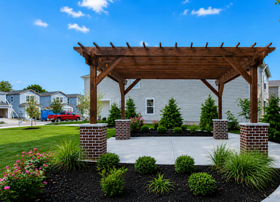 A wooden pergola is over a landscaped area.