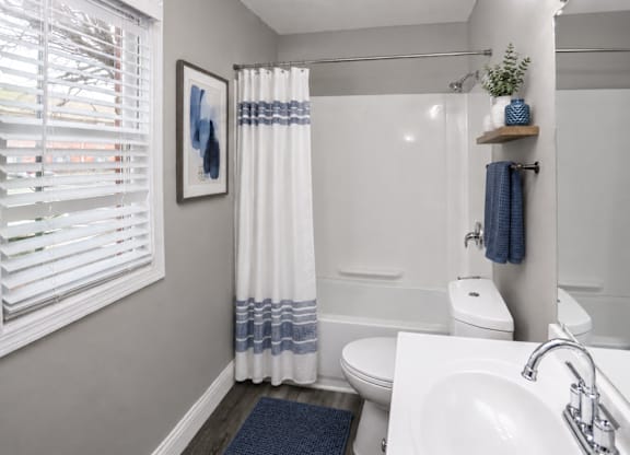 A bathroom with a white sink, toilet, and bathtub with blue and white curtains.