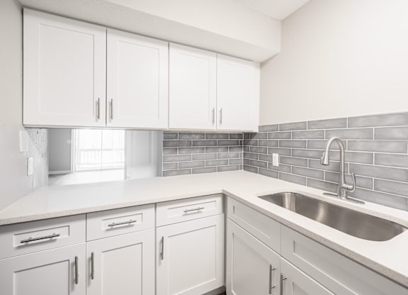A kitchen with white cabinets and a grey backsplash.