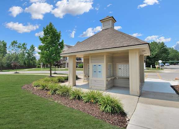 A small building with a brown roof and a signboard is surrounded by a well-maintained lawn.