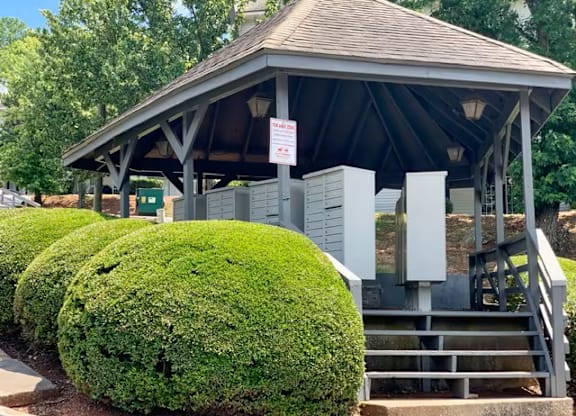 A small building with a roof and a signboard is surrounded by green bushes.