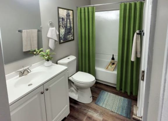 Bathroom with a mirror, vanity lights, a bathtub, a toilet, and a sink with white countertops. 