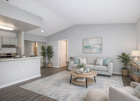 A living room with a grey couch, a coffee table, and a painting on the wall at Aqua Bay Apartments in Naples, FL 34116