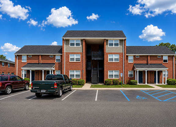 A parking lot in front of a brick building with a truck and a car parked.