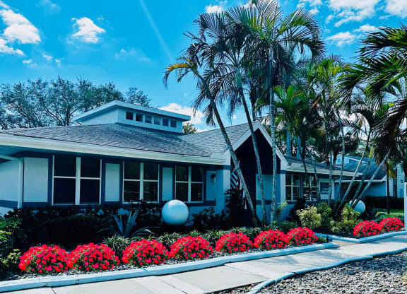 A house with palm trees and red flowers in front of it at Aqua Bay Apartments in Naples, FL 34116