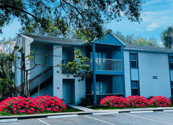 A blue apartment building with a parking lot and flowers at Aqua Bay Apartments in Naples, FL 34116
